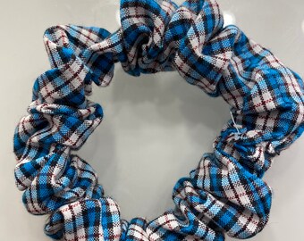 May include: A blue, white, and black plaid scrunchie. The fabric is gathered and elasticized, creating a ruffled effect. The scrunchie is a hair accessory, perfect for adding a touch of style to any hairstyle.