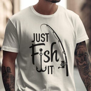 Puede incluir: Camiseta blanca con la frase negra "JUST Fish IT" y un diseño de caña de pescar y anzuelo. El diseño está centrado, ideal para los entusiastas de la pesca.