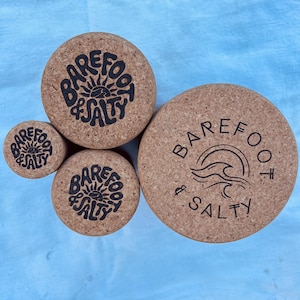 May include: Three cork containers with the logo "Barefoot & Salty" printed on them. The largest container has a wave design, the medium container has a sun design, and the smallest container has a sun design.