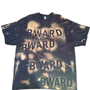 May include: A black short-sleeve t-shirt featuring a bleach-dyed effect with light tan splatter patterns. The word "BWARD" is printed in a bold, dark font across the chest four times in a stacked arrangement, contrasting against the bleached areas.