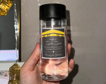 May include: A clear plastic bottle with a black lid and a label that says "A gift of Zam Zam. The purest water from us to you. Remember us in your duas. Parvez & Habiba".