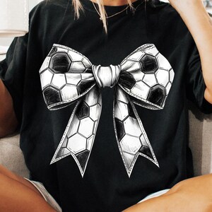 Op de afbeelding: Zwart T-shirt met een groot strikdesign gemaakt van voetballen. De strik is gedetailleerd met zwart-witte panelen, wat contrasteert met de donkere stof. Het shirt heeft een casual stijl.