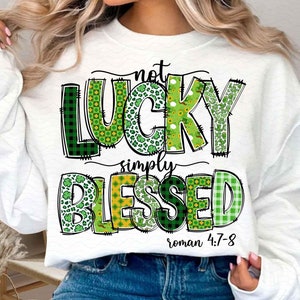 Puede incluir: Sudadera blanca con un diseño de patchwork verde, amarillo y negro que dice "not lucky simply blessed roman 4:7-8".