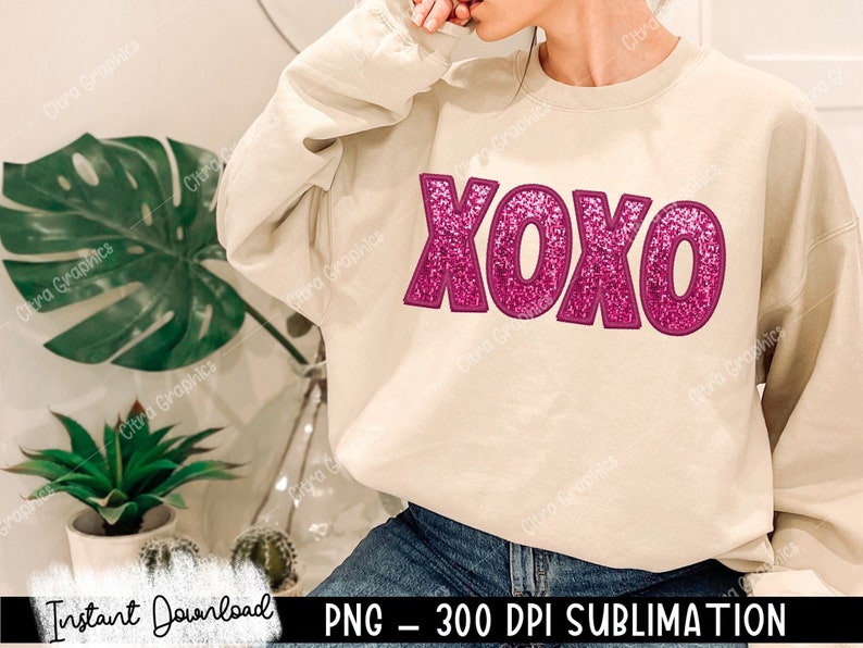 May include: A beige sweatshirt with a pink glitter XOXO graphic. The sweatshirt is a sublimation design, which means the graphic is printed directly onto the fabric.