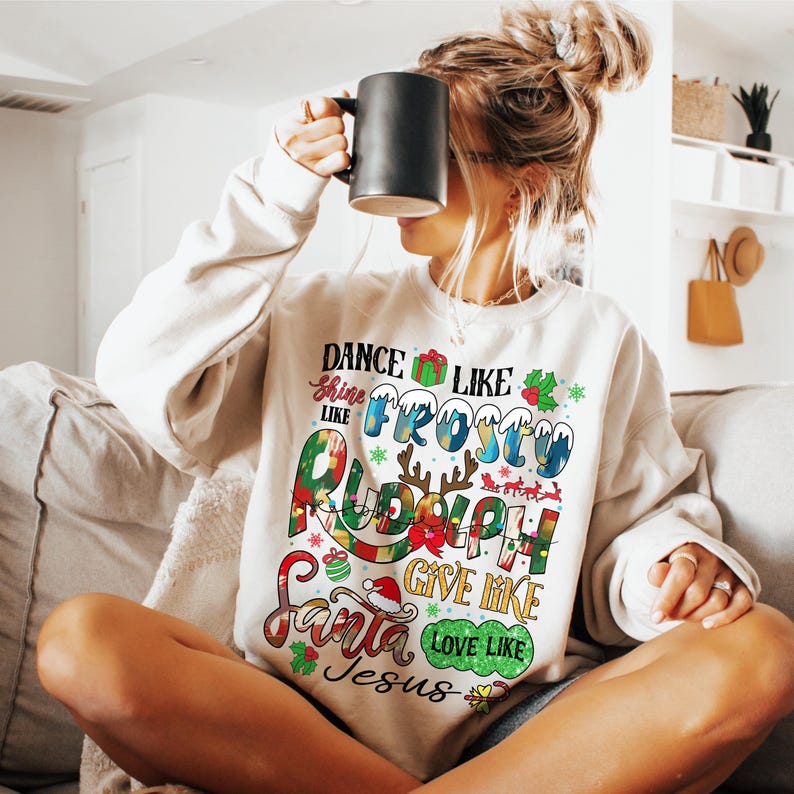 Op de afbeelding: Een wit sweatshirt met een kerstthema. De tekst op het sweatshirt luidt "Dance like Frosty, Shine like Rudolph, Give like Santa, Love like Jesus".