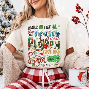 Op de afbeelding: Een wit T-shirt met een kerstthema. De tekst op het shirt luidt "Dance like Frosty, Shine like Rudolph, Give like Santa, Love like Jesus".