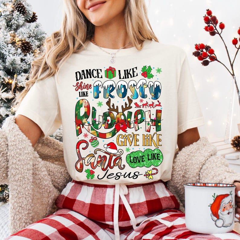 Op de afbeelding: Een wit T-shirt met een kerstthema. De tekst op het shirt luidt "Dance like Frosty, Shine like Rudolph, Give like Santa, Love like Jesus".