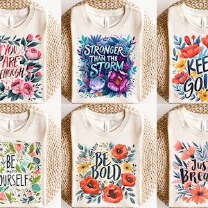 Peut inclure: Six t-shirts différents avec des motifs floraux et des textes motivants. Les t-shirts sont tous blancs avec une variété de fleurs et de feuilles colorées. Le texte sur les t-shirts comprend "You are enough", "Stronger than the storm", "Keep going", "Be yourself", "Be bold", et "Just breathe".