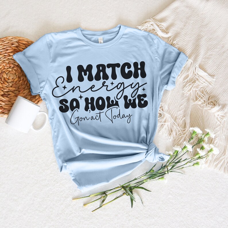 May include: Light blue t-shirt with black text that reads "I match energy so holla we gon' act today".