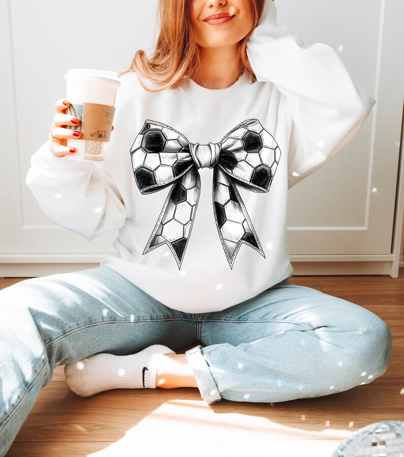 Op de afbeelding: Wit sweatshirt met een groot zwart-wit voetbalstrikontwerp. De strik is gedetailleerd met zeshoekige patronen en een lintachtige vorm. Een casual, alledaags kledingstuk.