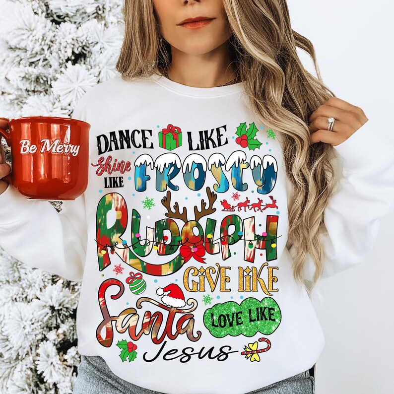 Op de afbeelding: Witte kersttrui met kleurrijke tekst die "Dance like Frosty, Shine like Rudolph, Give like Santa, Love like Jesus" zegt.