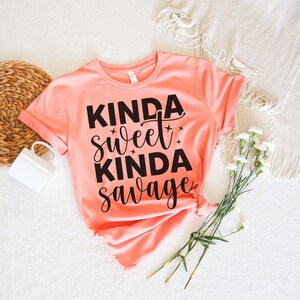 May include: A peach colored t-shirt with the text "Kinda sweet kinda savage" printed in black.