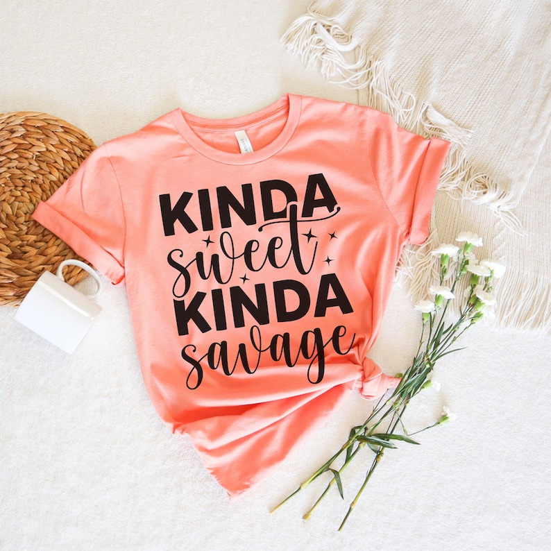 May include: A peach colored t-shirt with the text "Kinda sweet kinda savage" printed in black.
