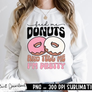 May include: White sweatshirt with a graphic design of two donuts and the text "feed me donuts and tell me I'm pretty".