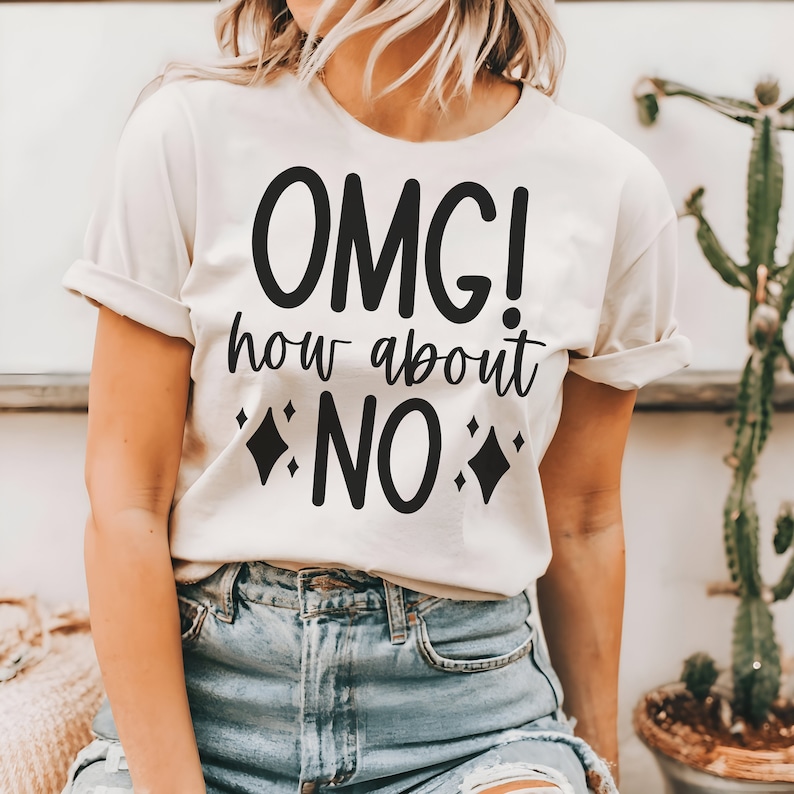 May include: A cream-coloured t-shirt featuring the text "OMG! how about NO" in black. The design includes diamond shapes. The shirt is worn with blue denim shorts.