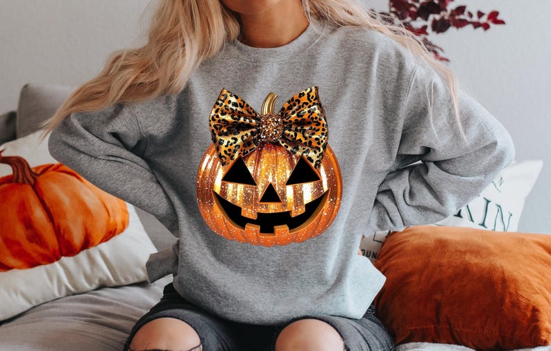 May include: A gray sweatshirt with a glittery orange pumpkin with a leopard print bow. The pumpkin has a jack-o-lantern face.