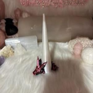 Puede incluir: Una vela cónica blanca con dos figuras de dragones rosas y negras unidas a la base.