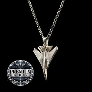 May include: A silver-toned rhodium-plated necklace featuring a fighter jet pendant suspended from a matching link chain. A circular emblem is visible in the corner with the text OSCAR BRAVO STUDIO PREMIUM SERIES RHODIUM PLATED.
