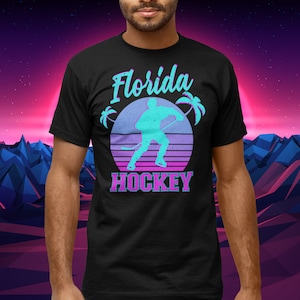 Puede incluir: Camiseta negra con un gr&aacute;fico de estilo retro de un jugador de hockey frente a una puesta de sol con palmeras. El texto "Florida Hockey" est&aacute; impreso debajo del gr&aacute;fico.
