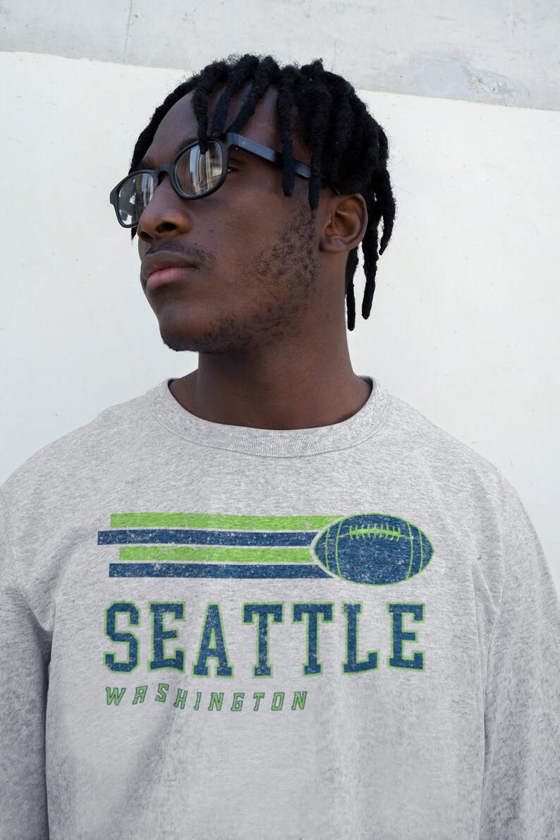 May include: A gray sweatshirt with a vintage-style graphic of a football and the text "SEATTLE WASHINGTON". The graphic is in green, blue, and white.