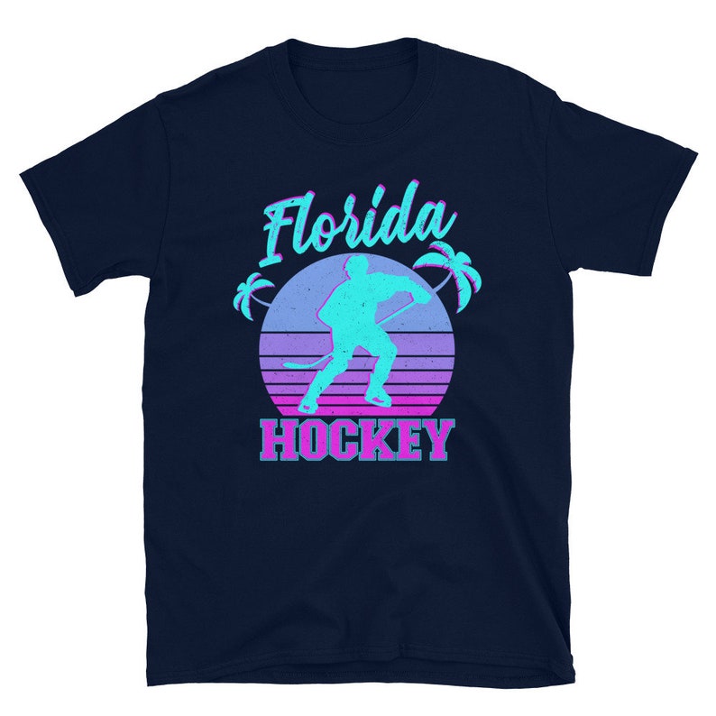 Puede incluir: Una camiseta azul marino con un gr&aacute;fico retro de un jugador de hockey frente a una puesta de sol con palmeras. El texto "Florida Hockey" est&aacute; impreso debajo del gr&aacute;fico.