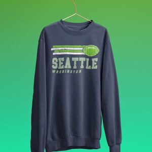 May include: A navy blue sweatshirt with a green and white graphic design that says "Seattle Washington" with a football graphic.