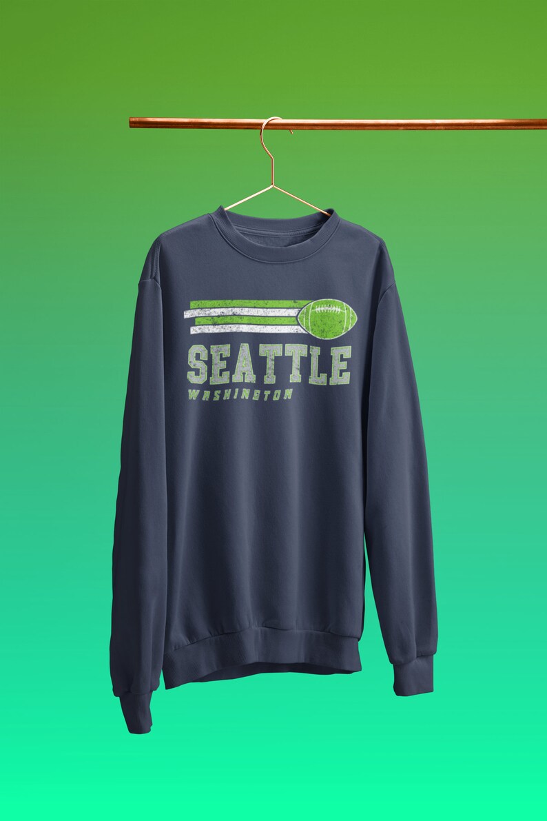 May include: A navy blue sweatshirt with a green and white graphic design that says "Seattle Washington" with a football graphic.