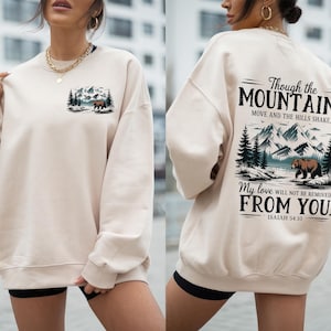 Może przedstawiać: Kremowa bluza z nadrukiem graficznym przedstawiającym niedźwiedzia i góry. Tekst na plecach brzmi "Though the Mountains Move and the Hills Shake, My love will not be removed from you. Isaiah 54:10"