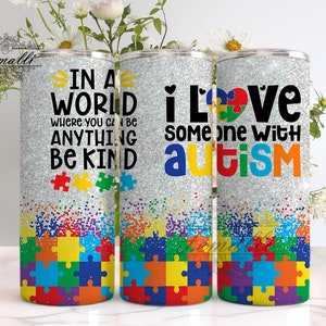 May include: Three silver glitter tumblers with a jigsaw puzzle design. The tumblers have the text "In a world where you can be anything be kind" on one, "I love someone with autism" on another, and a jigsaw puzzle heart on the third.