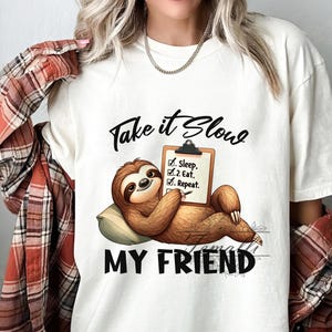May include: White t-shirt with a sloth illustration and the text "Take it slow my friend". The sloth is holding a clipboard with a checklist that says "1. Sleep, 2. Eat, 3. Repeat."