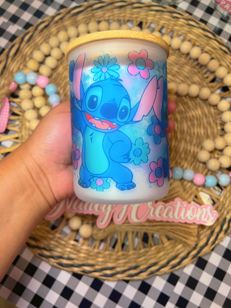May include: A blue and white ceramic jar with a bamboo lid features a cartoon character with blue fur and large ears. The character is surrounded by pink and blue flowers. The jar is sitting on a woven surface.