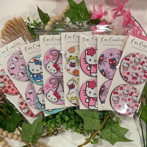May include: Six sets of round car coasters featuring Hello Kitty designs. Each set includes two coasters with different Hello Kitty patterns. The coasters are made of a white material with a pink border and are packaged in clear plastic bags.