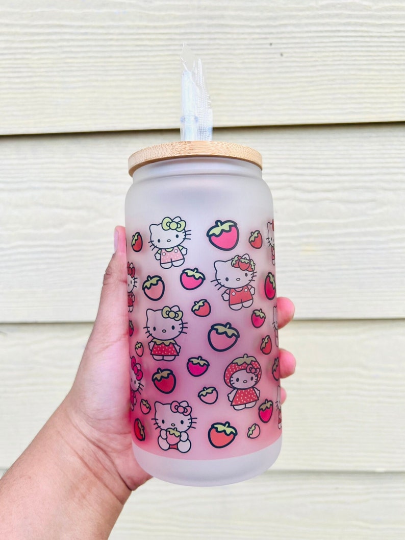 Puede incluir: Una botella de agua de vidrio esmerilado con tapa de bamb&uacute; y dise&ntilde;o de Hello Kitty y fresas. La botella tiene una pajita.