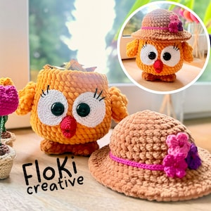 Puede incluir: Contenedor con forma de búho tejido a ganchillo y sombrero a juego. El búho es naranja con ojos blancos, pupilas negras y pico rojo. El sombrero es marrón con detalles florales rosas y morados. El texto "Floki creative" está abajo.