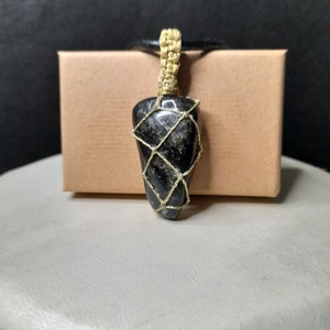 Amulet of Serpentine stone, uneven in shape, resembling a cone. The black color of the stone has a natural pattern of beige inclusions. The pendant is braided with golden waxed thread. The size is 4x2x1cm (high x top width x bottom width), weight 16g