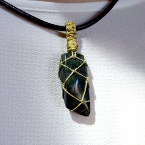 Amulet of Serpentine stone, uneven in shape, resembling a cone. The black color of the stone has a natural pattern of beige inclusions. The pendant is braided with golden waxed thread. The size is 4x2x1cm (high x top width x bottom width), weight 16g