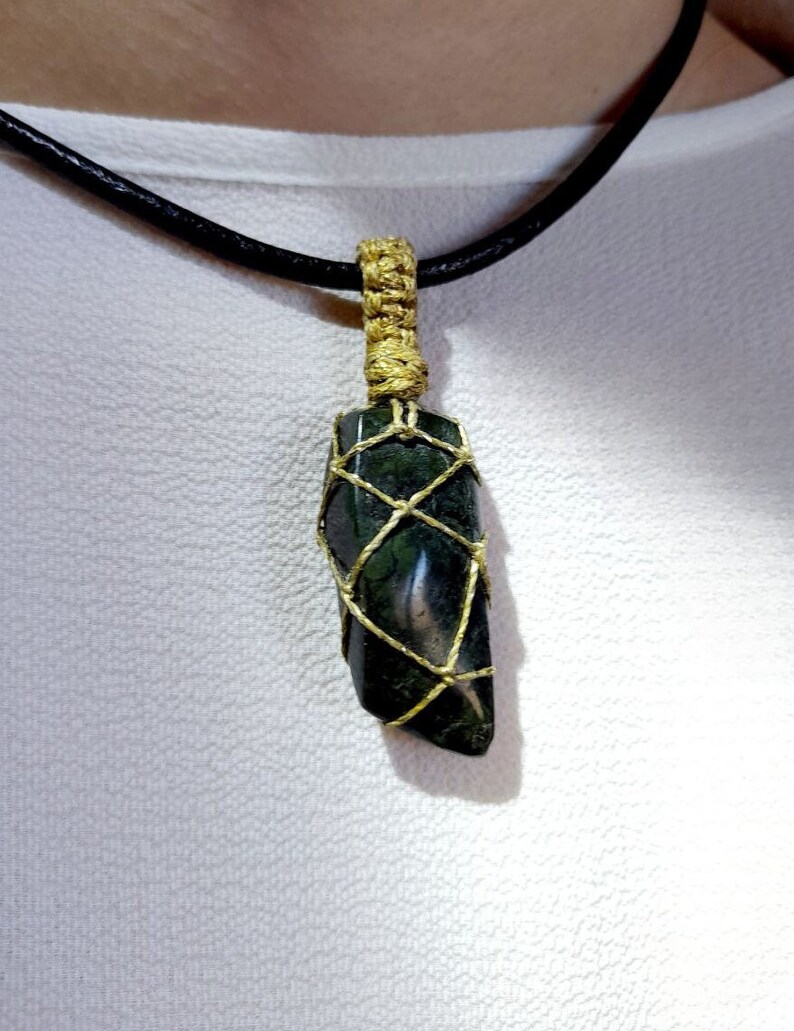 Amulet of Serpentine stone, uneven in shape, resembling a cone. The black color of the stone has a natural pattern of beige inclusions. The pendant is braided with golden waxed thread. The size is 4x2x1cm (high x top width x bottom width), weight 16g