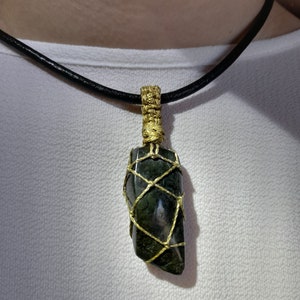 Amulet of Serpentine stone, uneven in shape, resembling a cone. The black color of the stone has a natural pattern of beige inclusions. The pendant is braided with golden waxed thread. The size is 4x2x1cm (high x top width x bottom width), weight 16g