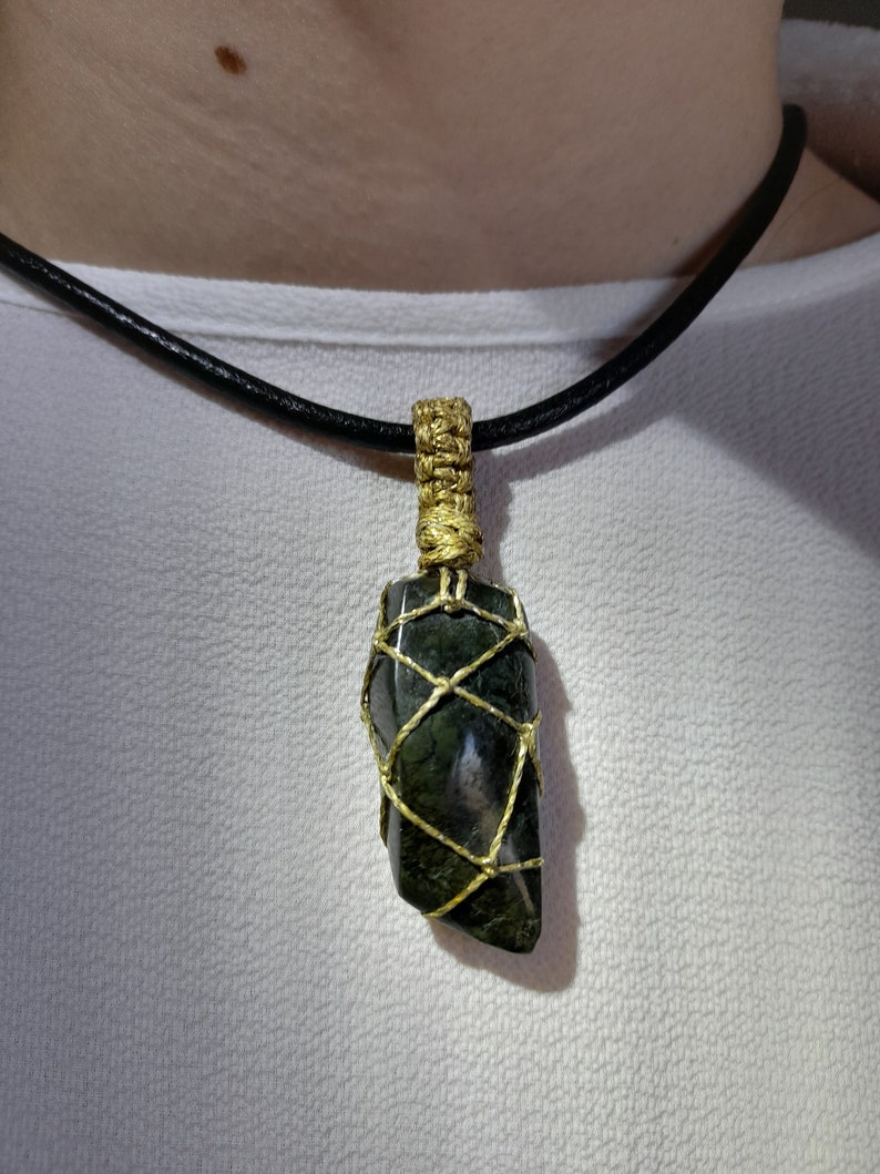 Amulet of Serpentine stone, uneven in shape, resembling a cone. The black color of the stone has a natural pattern of beige inclusions. The pendant is braided with golden waxed thread. The size is 4x2x1cm (high x top width x bottom width), weight 16g