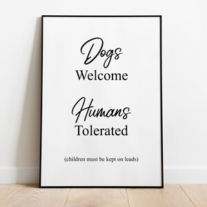 May include: Black and white framed sign with the text "Dogs Welcome Humans Tolerated (children must be kept on leads)"