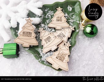Puede incluir: Seis adornos de árbol de Navidad de madera con diferentes frases de temática navideña: "decorar galletas", "donar un regalo", "cantar villancicos", "empaquetar regalos", "hornear galletas para Santa" y "[texto indescifrable]". Los adornos están en un plato verde con nieve artificial blanca.
