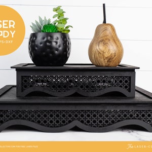 May include: Two black tiered display stands with a woven pattern and scalloped edges. A small potted succulent plant and a wooden pear are on the top tier.