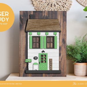 May include: A wooden sign with a white house cutout featuring a green door, green shutters, and a green mailbox. The house has a brown roof and a sign that says "LUCKY". The sign is on a brown wooden background.