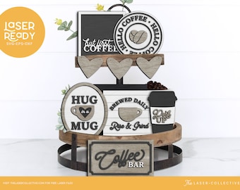 Peut inclure: Un plateau en bois à deux étages avec diverses décorations sur le thème du café, dont une pancarte qui dit "Coffee Bar", une pancarte ronde qui dit "Brewed Daily Rise & Grind", une pancarte ronde qui dit "Hug in a Mug", une pancarte ronde qui dit "Hello Coffee", et une tasse à café avec le texte "Perk Up".