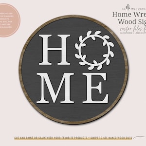 May include: A round, gray wooden sign with a white wreath and the word "HOME" in white letters. The sign is perfect for a farmhouse or rustic decor style.
