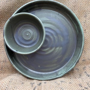 May include: A handmade ceramic serving set with a dark blue-green glaze. The set includes a large plate and a smaller bowl, both with a spiral design in the centre. The edges have a darker green hue.