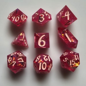 May include: A set of nine pink dice with white numbers. The dice are made of a translucent material with a glittery finish. The numbers on the dice are 1, 2, 3, 4, 5, 6, 7, 8, 9, 10, 11, 12, 13, 14, 15, 16, 17, 18, 19, 20, 21, 22, 23, 24, 25, 26, 27, 28, 29, 30, 31, 32, 33, 34, 35, 36, 37, 38, 39, 40, 41, 42, 43, 44, 45, 46, 47, 48, 49, 50, 51, 52, 53, 54, 55, 56, 57, 58, 59, 60.