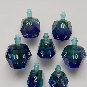 Puede incluir: Siete juegos de dados poliédricos con forma de botella, hechos de resina translúcida azul y verde. Cada dado tiene números blancos y un tapón azul claro. Los dados están diseñados para juegos de rol de mesa.