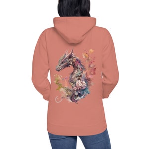 Könnte beinhalten: Ein korallenrosa Hoodie mit einer Aquarell-Illustration eines Drachen, der von Blumen umgeben ist, auf der Rückseite.