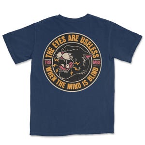 A traditional tattoo shirt featuring a panther with eyes in its mouth and the phrase “The eyes are useless when the mind is blind,” printed on a Comfort Colors tee for fans of tattoo art and alternative clothing.